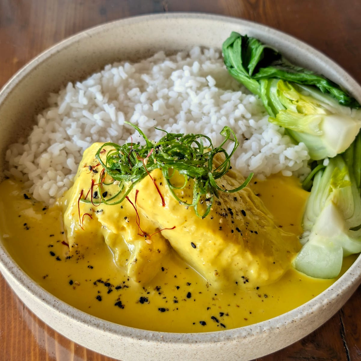 Bowl of food with rice, egg, and greens on a wooden surface