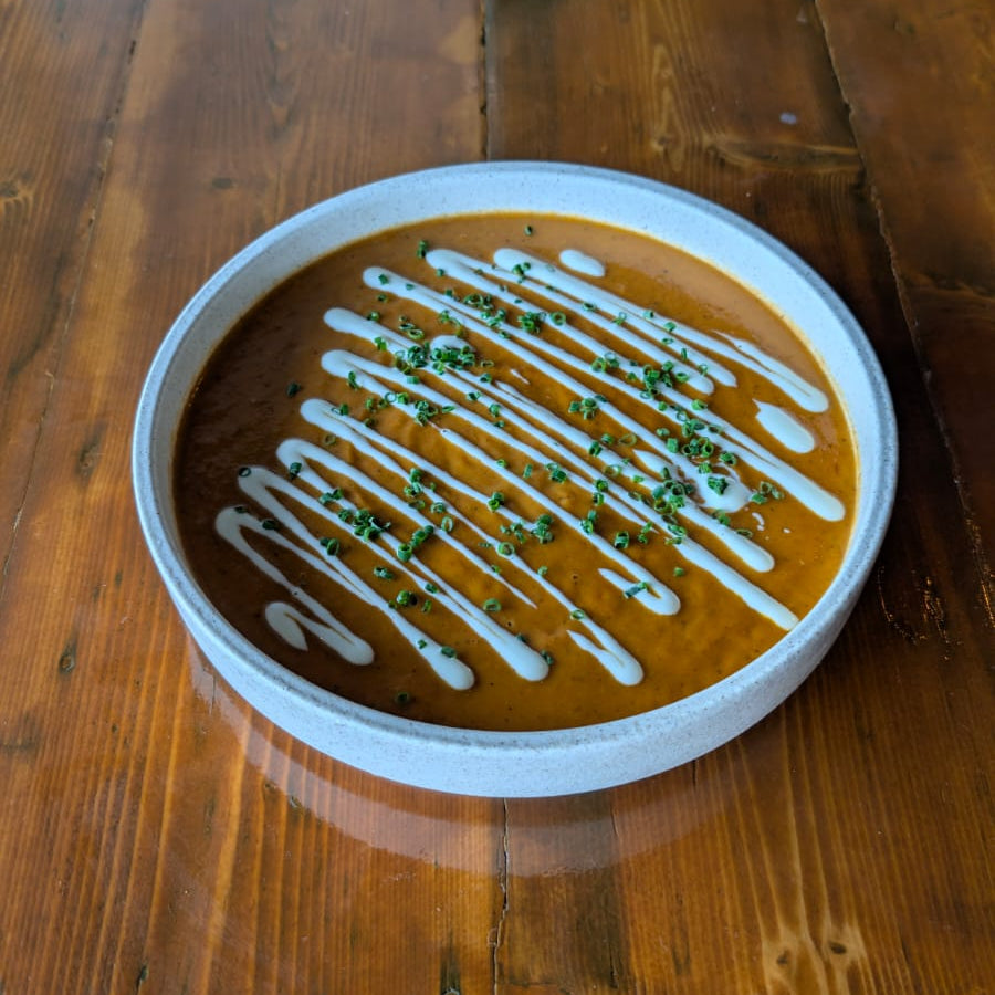 Summer tomato bisque plated up with a drizzle of cream, in a white bowl on a woodern table.